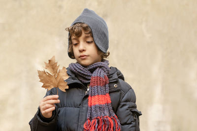 Cute boy holding dry leaf against wall