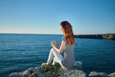 Woman sitting on rock by sea against clear sky