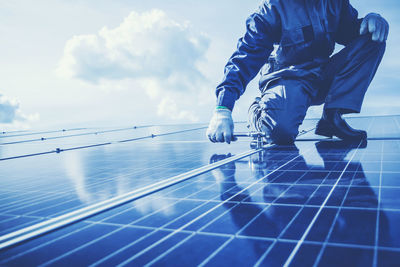 Low section of worker fitting solar panel against sky