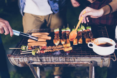 Friends preparing food on barbecue grill at night