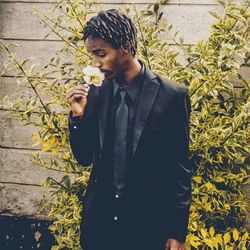 Young man smelling flower while standing against plants