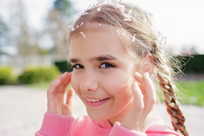 Emotional portrait of girl in pink hoodie with sakura petals on her head and eyelashes. spring vibes