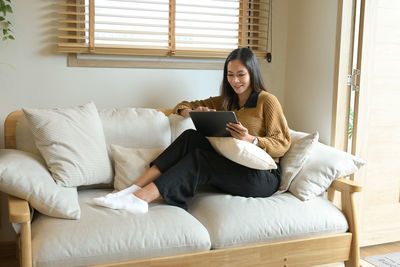 Young woman using phone while sitting on bed at home