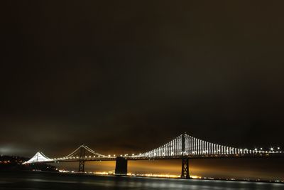Illuminated oakland bay bridge over san francisco bay against sky at night