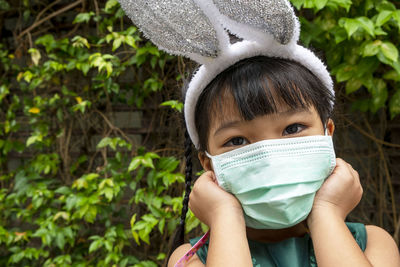 Portrait of cute girl wearing face mask against plants background.