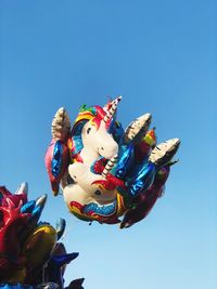 Low angle view of helium balloons against clear blue sky