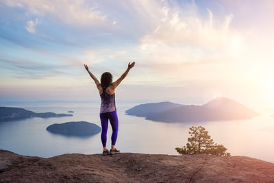 Rear view of woman standing on rock against sky