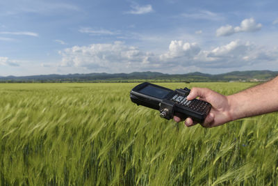 Cropped hand of engineer holding equipment on field against sky