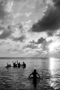 Silhouette friends in sea against sky during sunset