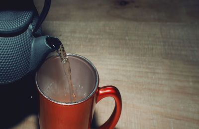 Pouring tea into a red cup on a wooden table. closeup. copy space.