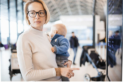 Mother traveling with child, holding his infant baby boy at airport terminal, checking flight