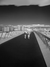 Rear view of female friends walking on bridge in city against sky