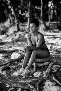 Portrait of young woman sitting on tree in forest