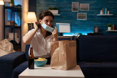 Portrait of young woman using mobile phone while sitting on sofa at home