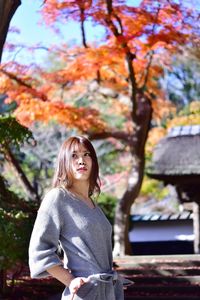 Portrait of smiling young woman standing against trees during autumn