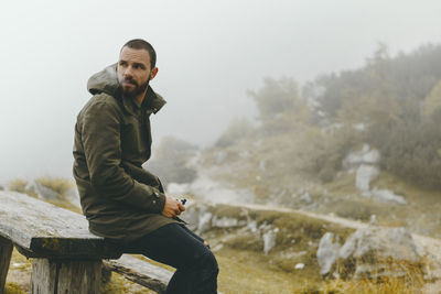 Young man smoking at table against landscape