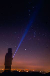 Digital composite image of silhouette man holding standing with illuminated flashlight against sky at night