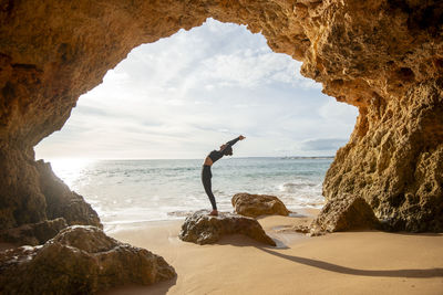 Fit, sporty woman doing a backbend exercise by the sea in a cave