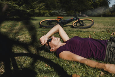 Woman lying on grass while resting by mountain bike at park