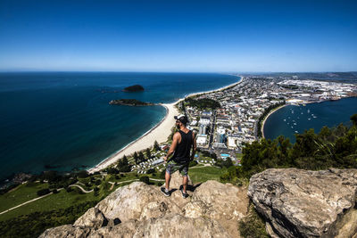 People standing on rock by sea against blue sky
