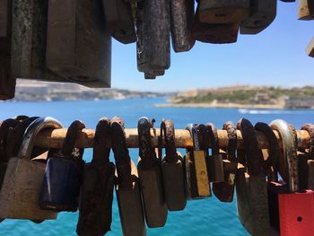 Close-up of padlocks hanging on metal by sea against sky