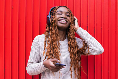 Portrait of smiling young woman using phone while standing against red wall