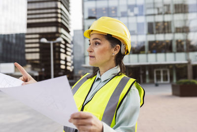 Architect wearing hardhat holding blueprint working outside modern building