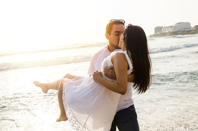 Couple kissing at beach against clear sky