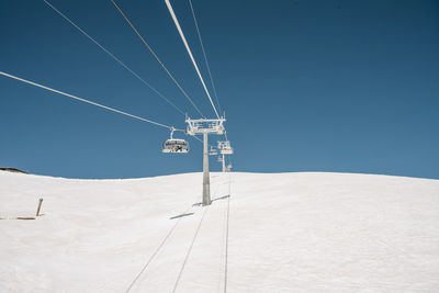 Electricity pylon on snow covered land against clear blue sky