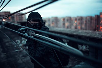 Portrait of man holding camera in city against sky