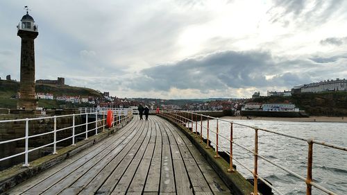 Footbridge over sea against cloudy sky
