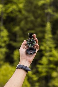 Cropped hand holding navigational compass against trees in forest