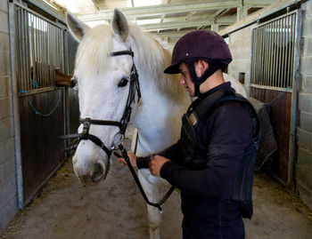 Young rider preparing horse for riding in stable