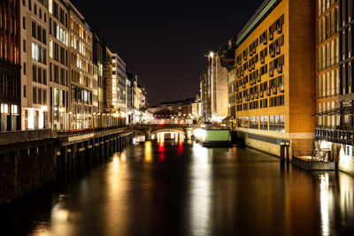 Canal amidst illuminated buildings in city at night