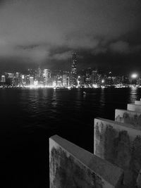 Illuminated cityscape by sea against sky at night