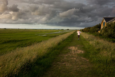 Woman walking on field against storm clouds