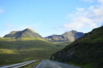 Road leading towards mountains against blue sky