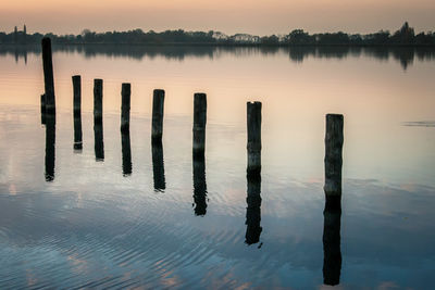 Wooden posts in lake against sky at sunset