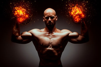 Digital composite image of shirtless man with fire against gray background