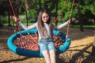 Portrait of a beautiful caucasian girl with a smile riding a round rope swing in a park