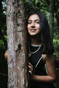 Close-up of young woman smiling while standing by tree trunk