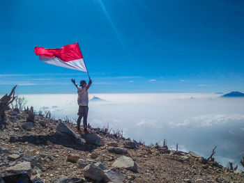 Man standing on rock at beach against blue sky