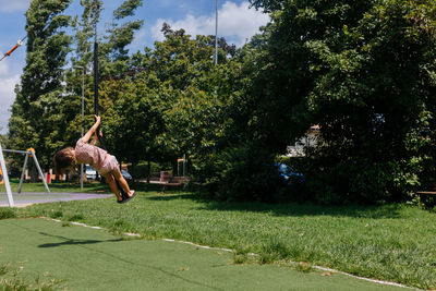 Rear view of woman exercising on field against trees