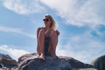 Young woman sitting on rock against sky