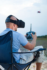Side view of mid adult man flying quadcopter while sitting on chair