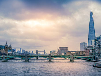 View of bridge over river in city against cloudy sky