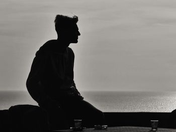 Man sitting at beach against sky