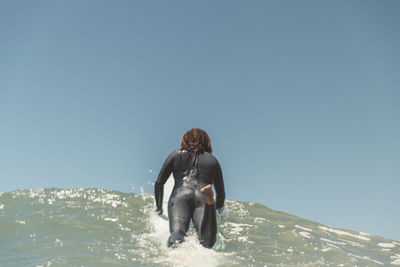 Black woman gping over a wave on her surfboard in the water