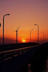 Silhouette street lights by sea against clear sky during sunset