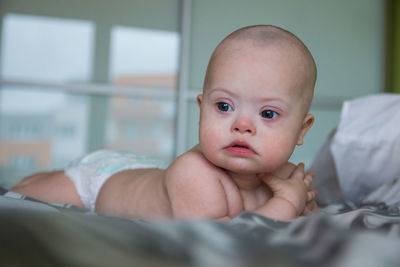 Cute baby boy looking away lying on bed at home